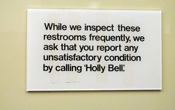 Sign outside bathroom asking patrons to report unsatisfactory conditions by calling "Holly Bell."